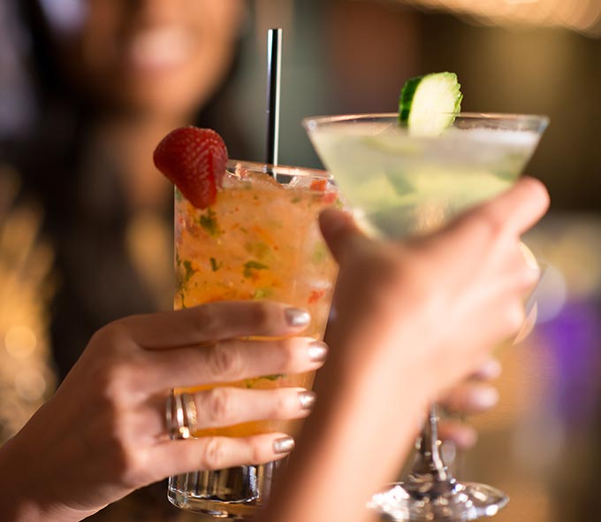 Closeup of Feminine Hands Holding Cocktails at Center Bar